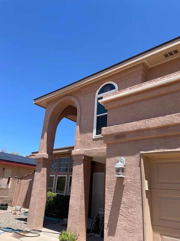 Two-story Albuquerque stucco home in midday sun, the permanent lighting channel reading as trim along the roofline and portal