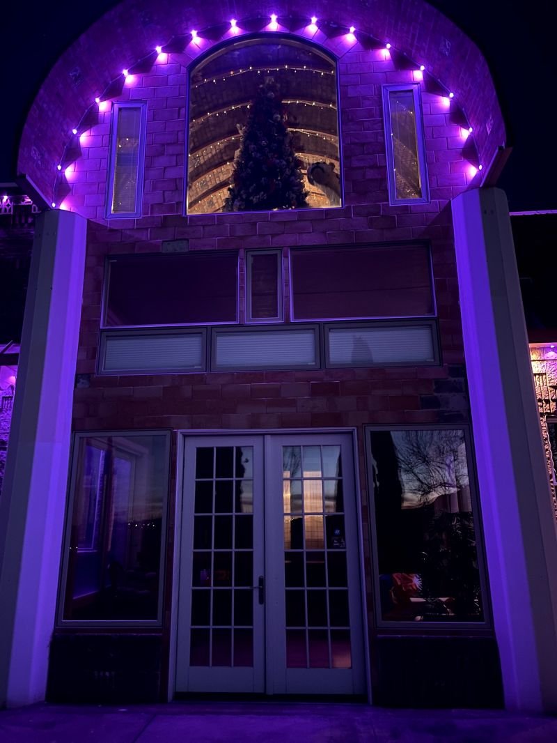 Permanent lighting tracing the arched entry and windows of a home at night