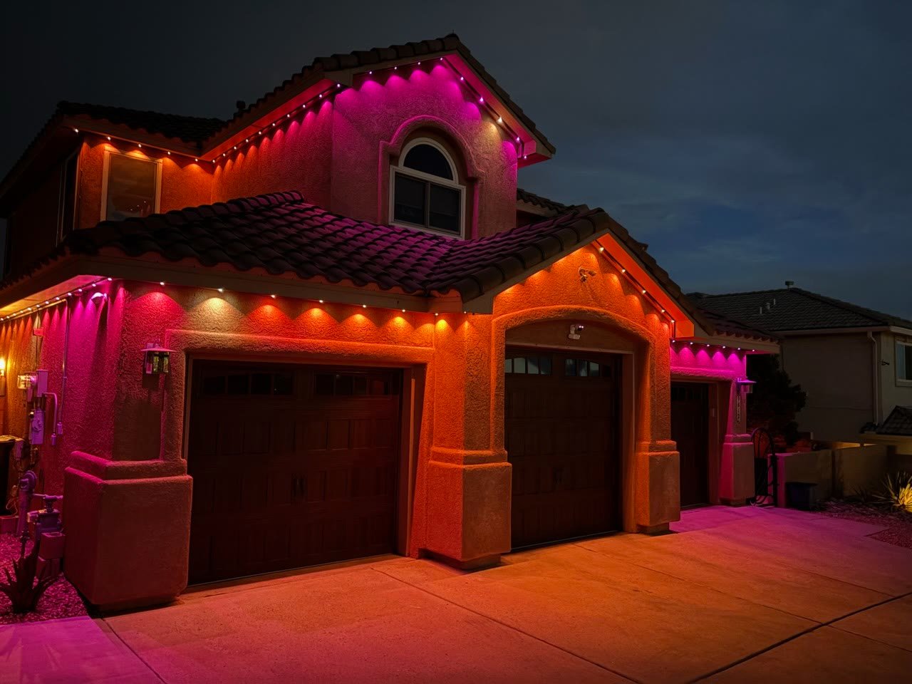 The same Albuquerque home from the same angle with the permanent lighting switched to a pink and orange scene