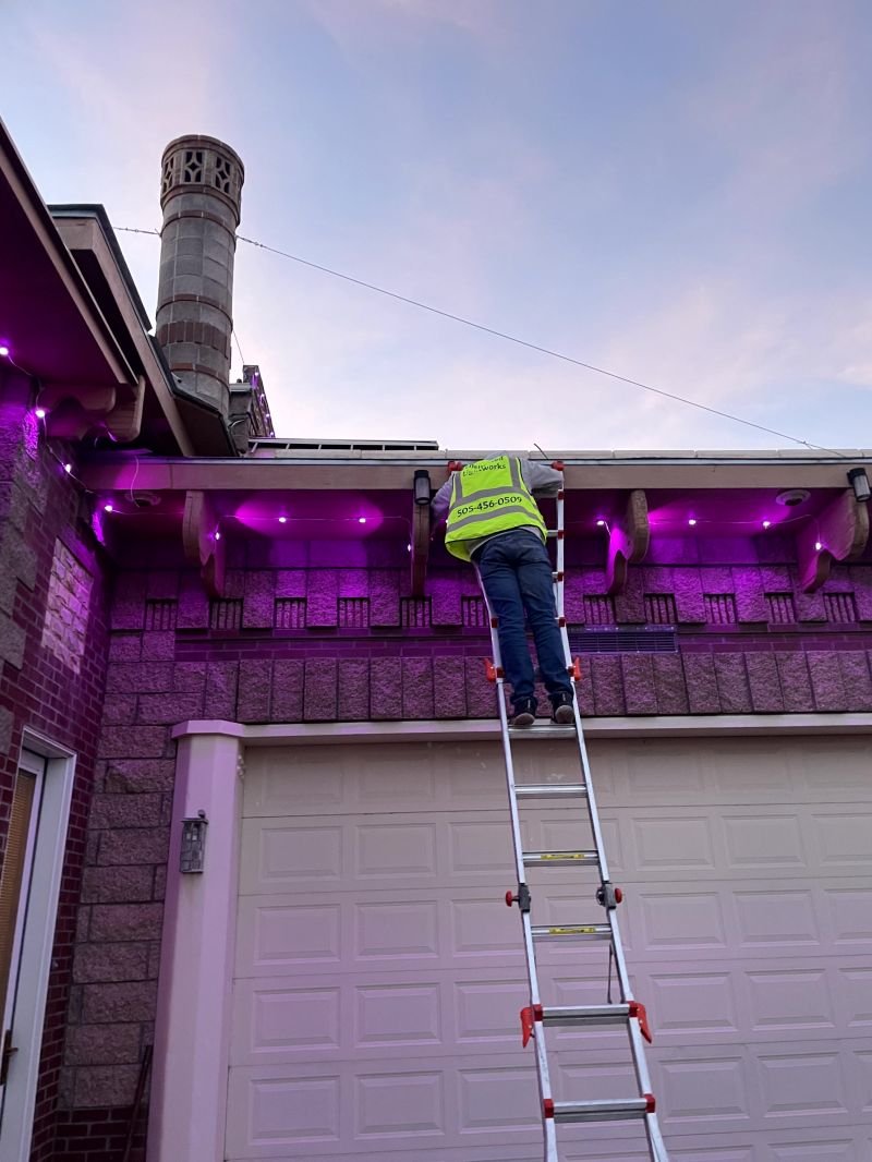 Installer on a ladder fitting permanent lighting under the eave of an Albuquerque home