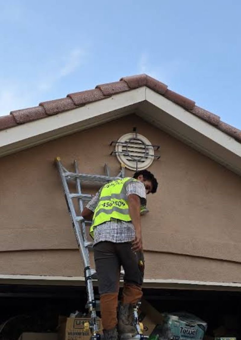 Installer on a ladder fitting permanent lighting under the tile roof edge of an Albuquerque home in daylight